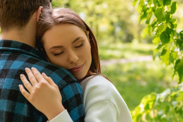 Молодая женщина с закрытыми глазами обнимает парня в парке — стоковое фото