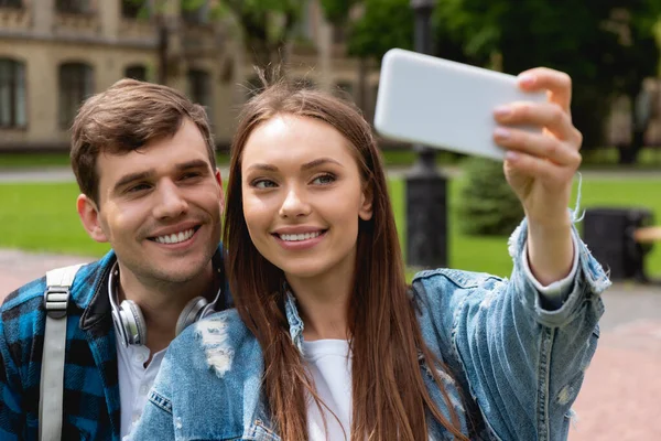 Selettiva messa a fuoco di allegro ragazza presa selfie con bello studente — Foto stock