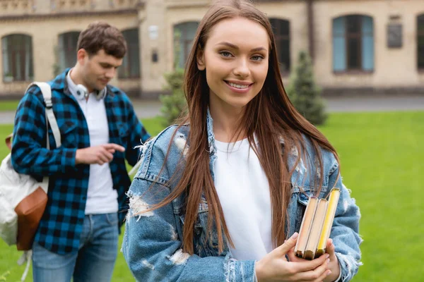 Foco seletivo de menina feliz segurando livros perto de estudante bonito — Fotografia de Stock