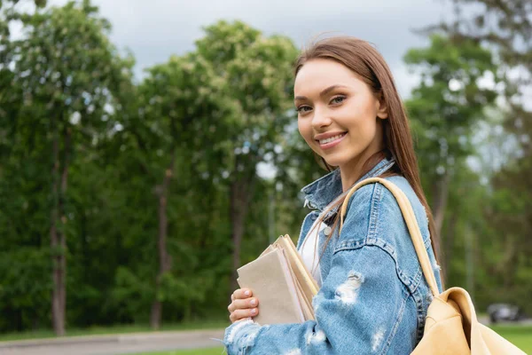 Estudiante alegre y atractivo mirando a la cámara y sosteniendo libros - foto de stock