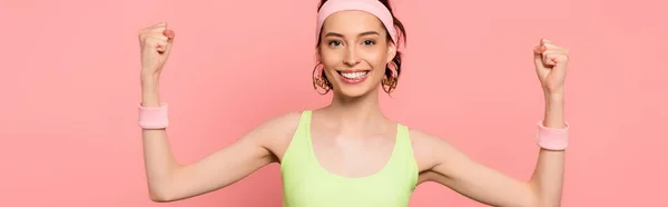 Panoramaaufnahme einer fröhlichen Sportlerin mit geballten Fäusten, die isoliert in die Kamera auf rosa blickt — Stockfoto