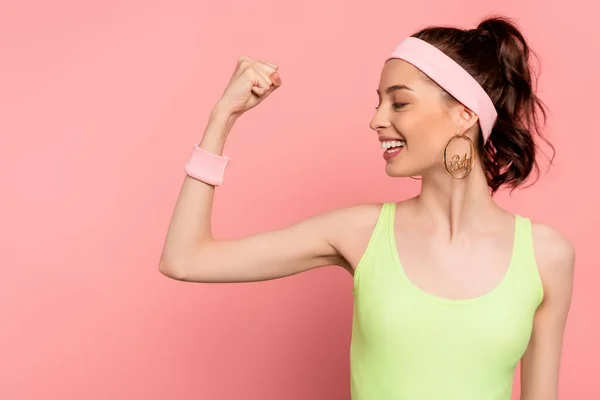 Deportista alegre con el puño cerrado mirando el músculo en rosa - foto de stock