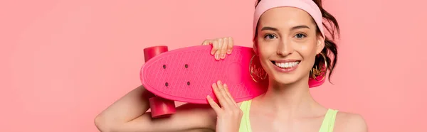 Panoramic concept of cheerful girl with headband holding penny board isolated on pink — Stock Photo