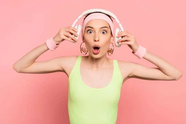 Jovem mulher chocada tocando fones de ouvido em rosa — Fotografia de Stock