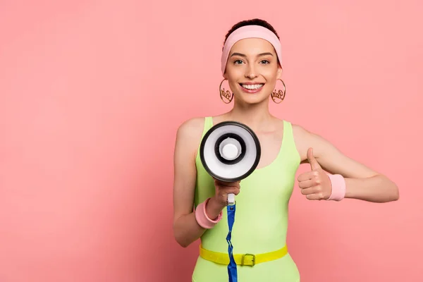 Glückliche junge Frau zeigt Daumen hoch und hält Lautsprecher auf rosa — Stockfoto