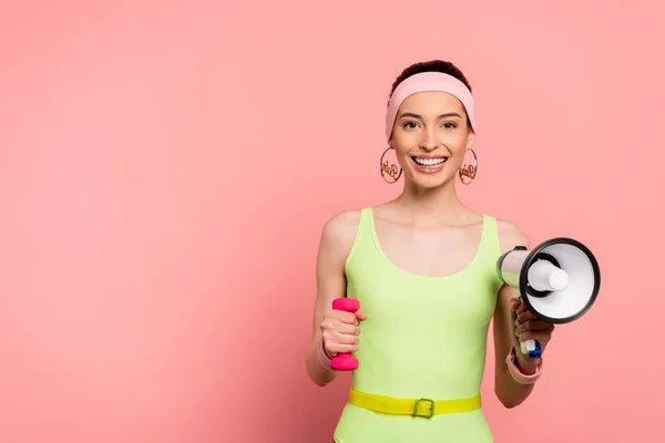 Happy sportswoman holding dumbbell and loudspeaker on pink — Stock Photo