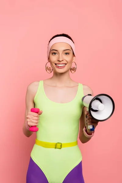 Cheerful sportswoman holding dumbbell and loudspeaker on pink — Stock Photo
