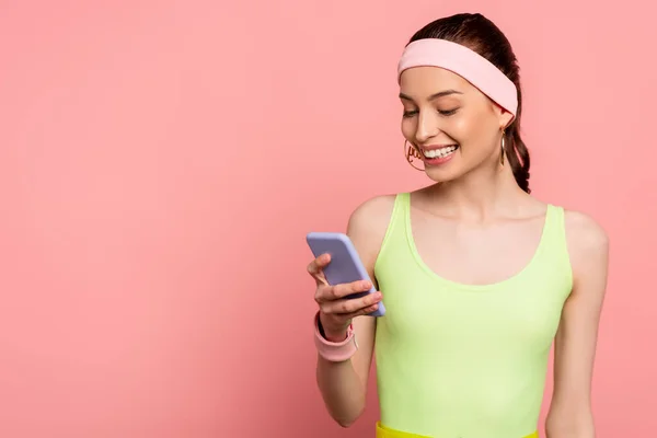 Mujer alegre en diadema usando teléfono inteligente aislado en rosa - foto de stock