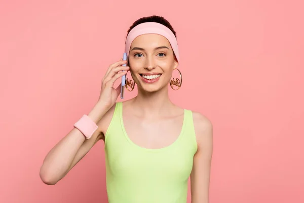 Cheerful woman in headband talking on smartphone isolated on pink — Stock Photo