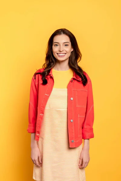 Счастливая молодая женщина стоит и улыбается на желтом — стоковое фото