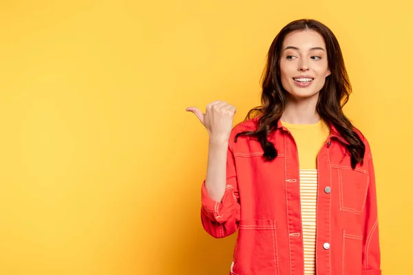 Fröhliche junge Frau zeigt mit dem Finger und schaut weg auf gelb — Stockfoto