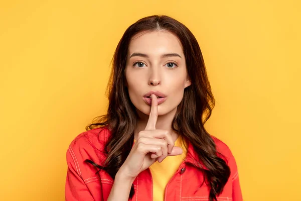 Young woman showing hush sign and looking at camera on yellow — Stock Photo