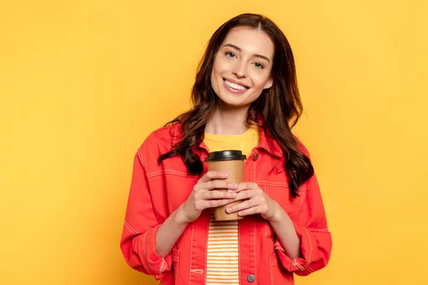 Alegre joven mujer sosteniendo taza de papel en amarillo - foto de stock