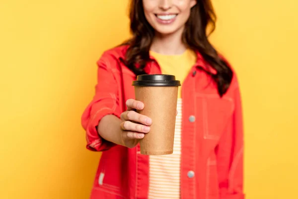 Селективное внимание веселой молодой женщины, держащей бумажную чашку на желтом — стоковое фото