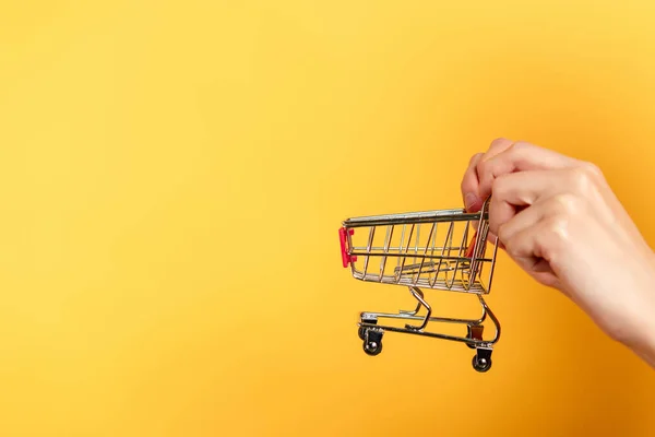 Ausgeschnittene Ansicht einer Frau mit kleinem Einkaufswagen auf gelb — Stockfoto