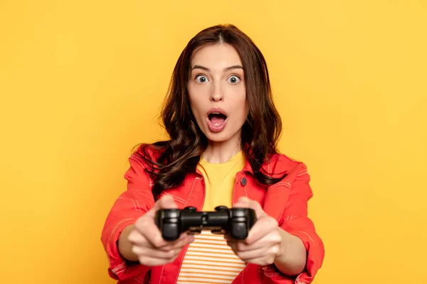 KYIV, UKRAINE - MAY 25, 2020: selective focus of surprised young woman holding joystick while playing video game isolated on yellow — Stock Photo