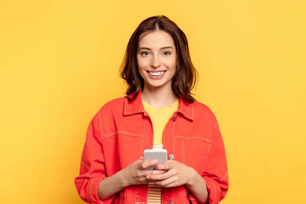 Feliz joven mujer sosteniendo teléfono inteligente aislado en amarillo - foto de stock