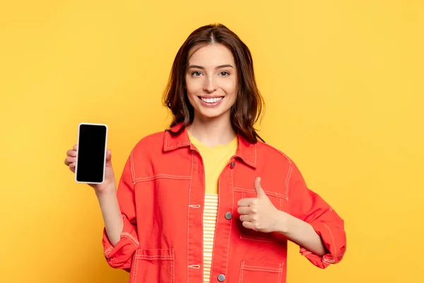Happy young woman holding smartphone with blank screen and showing thumb up on yellow — Stock Photo