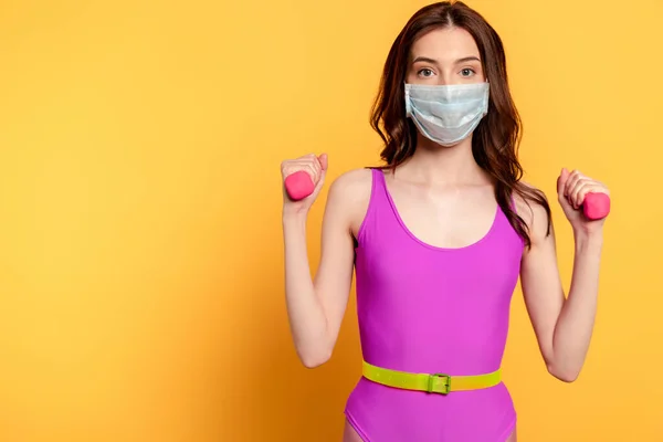 Young sportswoman in medical mask exercising with dumbbells on yellow — Stock Photo