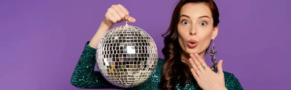 Panoramic concept of surprised young woman holding disco ball isolated on purple — Stock Photo