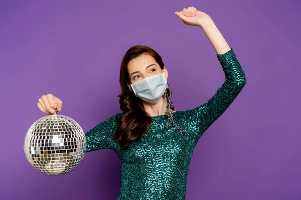 Женщина в платье и медицинская маска проведение диско мяч на фиолетовый — стоковое фото
