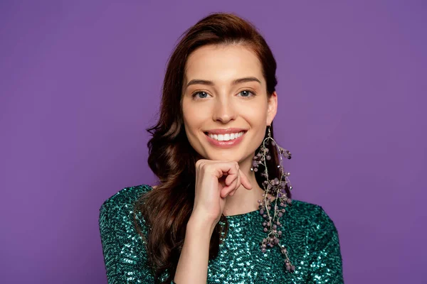 Happy young woman in dress touching face and looking at camera isolated on purple — Stock Photo
