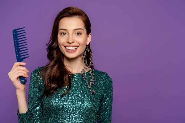 Alegre mujer sosteniendo peine y sonriendo aislado en púrpura - foto de stock