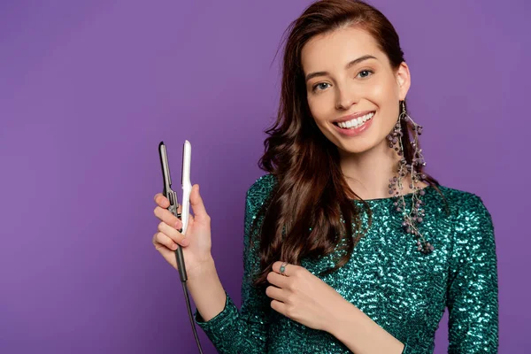 Весела жінка тримає маленьке випрямлення волосся ізольовано на фіолетовому — стокове фото