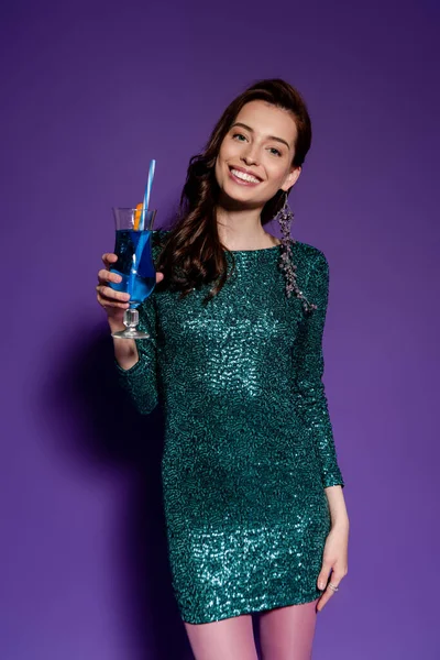 Alegre joven en vestido de fiesta celebración de vidrio con cóctel de alcohol en púrpura - foto de stock