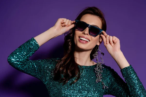 Mujer elegante tocando gafas de sol y sonriendo en púrpura - foto de stock