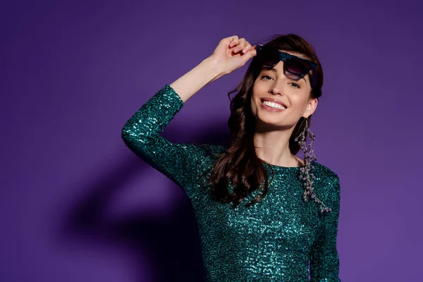 Mujer feliz tocando gafas de sol y sonriendo en púrpura - foto de stock