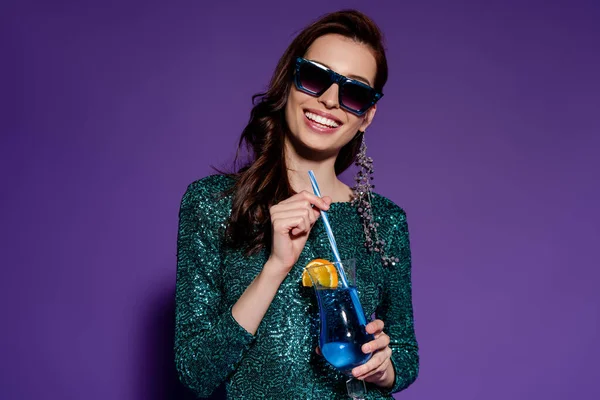 Glückliche Frau in Sonnenbrille mit Strohhalm und Glas mit Alkoholcocktail auf lila — Stockfoto