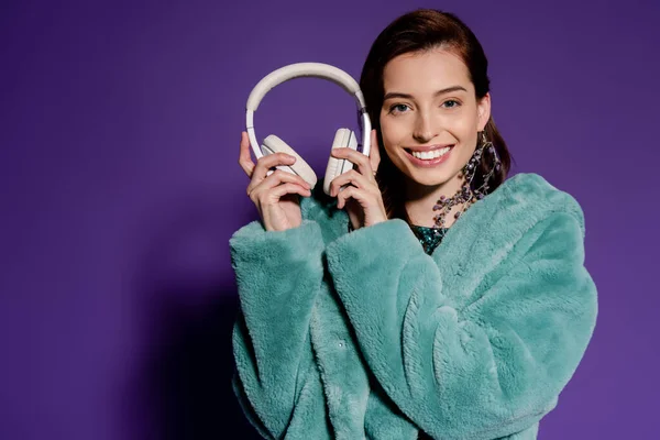 Happy young woman holding headphones on purple — Stock Photo