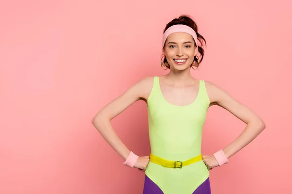 Glückliche junge Frau mit Stirnband, die Hände auf den Hüften auf rosa — Stockfoto