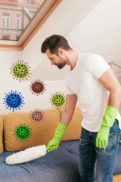 Side view of handsome man cleaning couch with dust brush in living room, bacteria illustration — Stock Photo