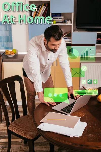 Hombre guapo en camisa y bragas usando portátil cerca de cereales en la mesa en la cocina, ilustración de la oficina en casa - foto de stock