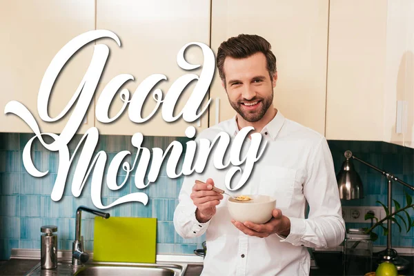 Hombre guapo sonriendo a la cámara mientras come cereales en la cocina, ilustración buenos días - foto de stock