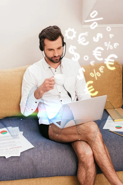 Télétravailleur en chemise et culotte boire du café tout en utilisant casque et ordinateur portable sur le canapé, illustration de signes de devise — Photo de stock