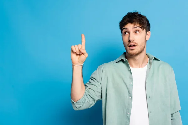 Nachdenklicher junger Mann zeigt mit dem Finger weg, während er auf blau schaut — Stockfoto