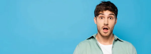 Horizontal image of shocked young man looking at camera isolated on blue — Stock Photo