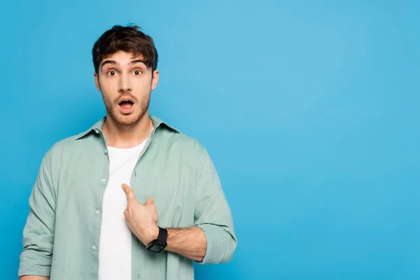 Sorprendido joven apuntando con el dedo a sí mismo aislado en azul - foto de stock