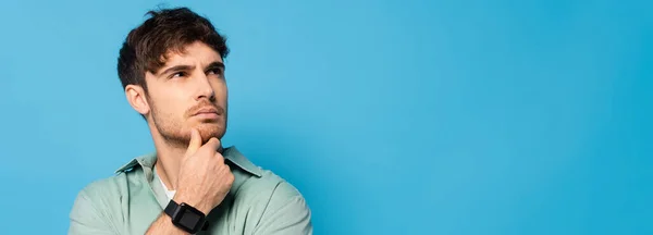 Horizontal image of thoughtful man touching chin while looking away isolated on blue — Stock Photo