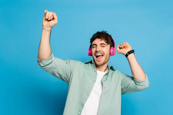 Allegro giovane ballando e cantando con gli occhi chiusi sul blu — Foto stock