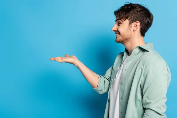 Side view of happy young man standing with open arm on blue — Stock Photo