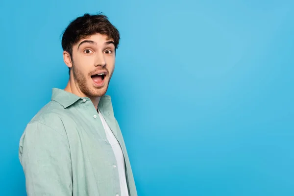 Shocked young man with open mouth looking at camera isolated on blue — Stock Photo