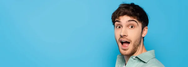 Horizontal image of excited young man looking at camera isolated on blue — Stock Photo