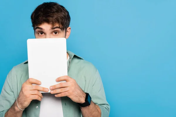 Effrayé jeune homme obscurcissant visage avec tablette numérique isolé sur bleu — Photo de stock