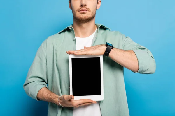 Ausgeschnittene Ansicht eines jungen Mannes, der ein digitales Tablet mit leerem Bildschirm auf blau zeigt — Stockfoto