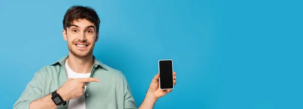 Website-Header eines glücklichen jungen Mannes zeigt auf Smartphone mit leerem Bildschirm auf blau — Stockfoto