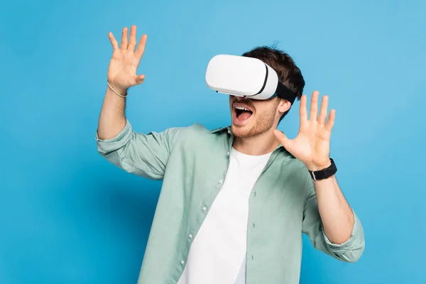 Excité jeune homme gestuelle tout en utilisant vr casque sur bleu — Photo de stock